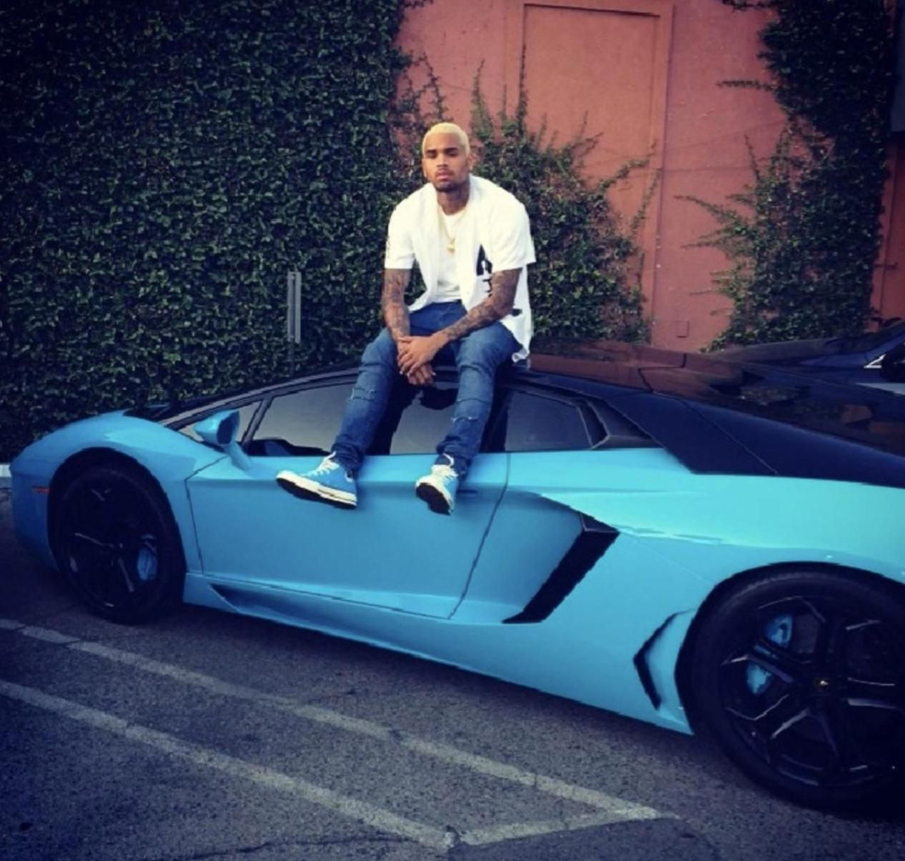 Chris Brown sitting atop a custom painted Miami Blue Lamborghini Aventador that recently sold on Cars and Bids