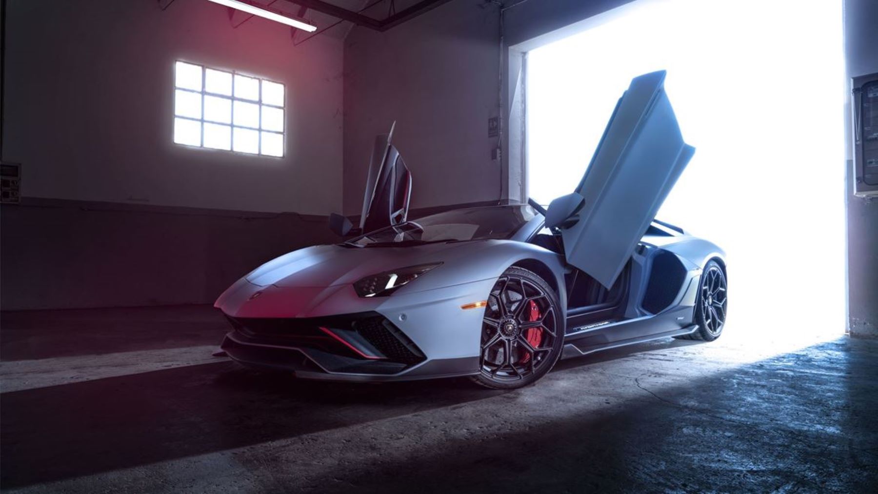 The Lamborghini Aventador Ultimae Ambient LP 780-4 with its doors open and bathed in light from outside its garage