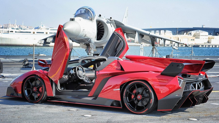 Red Lamborghini Veneno Roadster, the most expensive Lamborghini ever built, sitting in front of a fighter jet