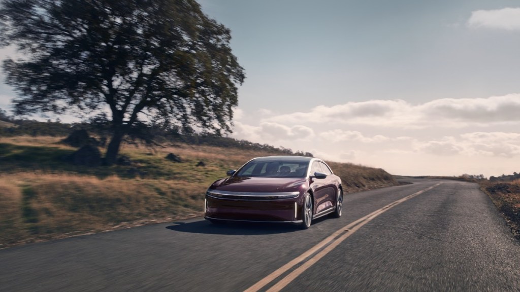 a red 2022 lucid air grand touring drives along a country road
