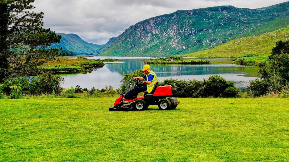Man mowing a lawn near a lake, highlighting how its bad to mow the grass on a lawn too short