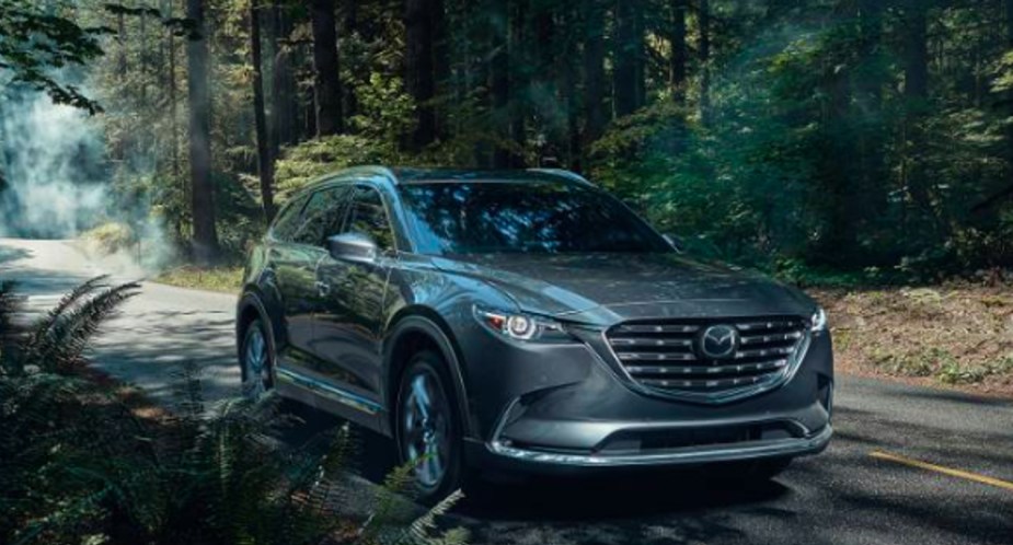 A gray 2022 Mazda CX-9 midsize SUV is driving on the road.