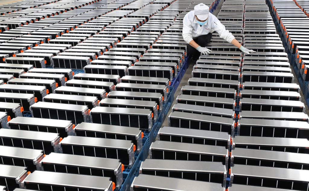 A worker in a Chinese factory sorts crates full of EV batteries.