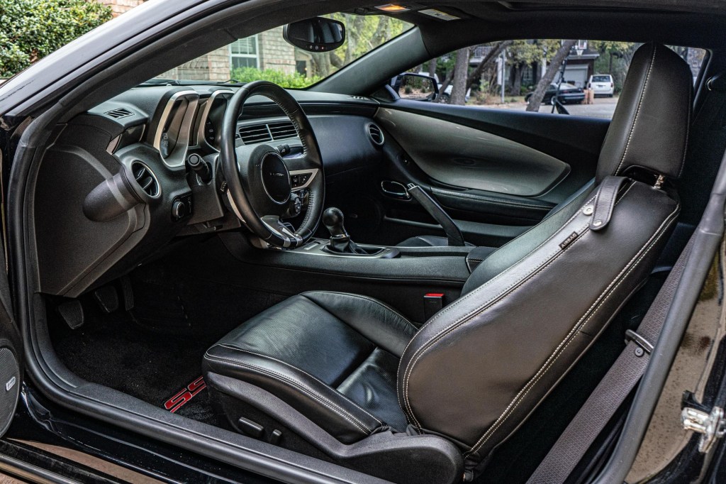The black-leather front sports seats and dashboard of a manual modified 2010 Chevrolet Camaro SS in a driveway