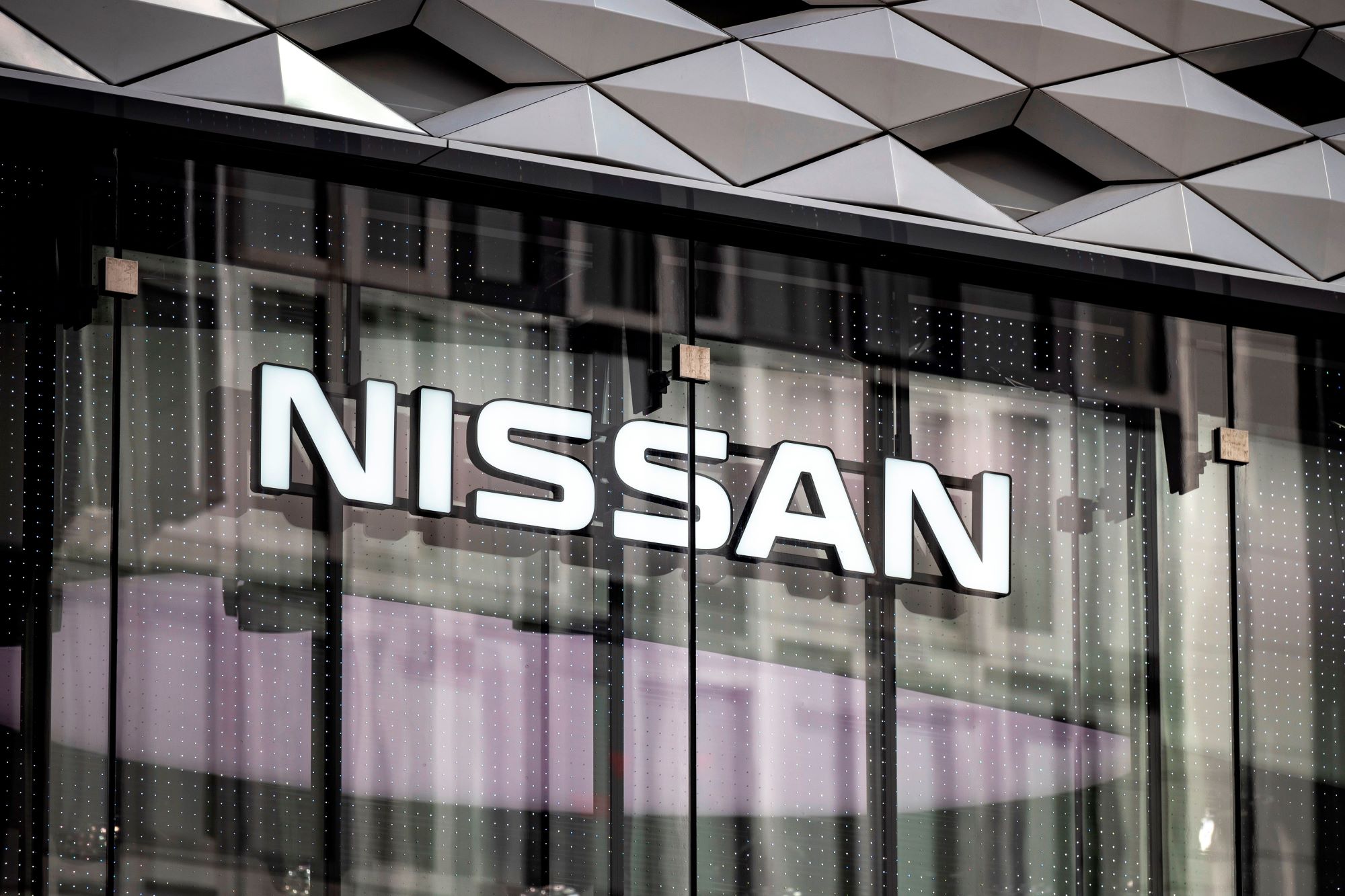 A building with tall glass doors and Nissan, who ensures the best new car smell, written on the side.