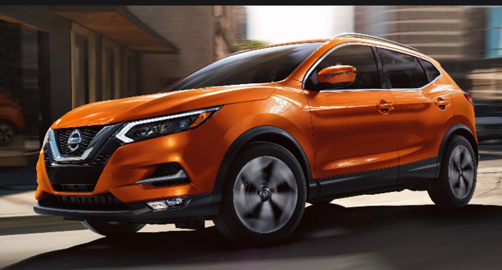An orange 2022 Nissan Rogue Sport small SUV is driving on the road. 