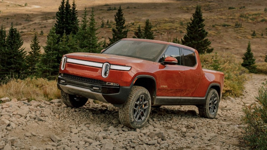 Orange 2022 Rivian R1T pickup truck, which has a 3-second 0-60 mph acceleration time, driving up a hill
