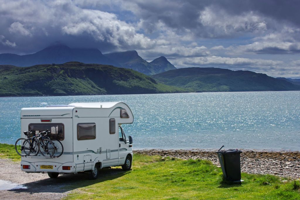 RV travelers parked in front of a body of water with mountains in the background. 