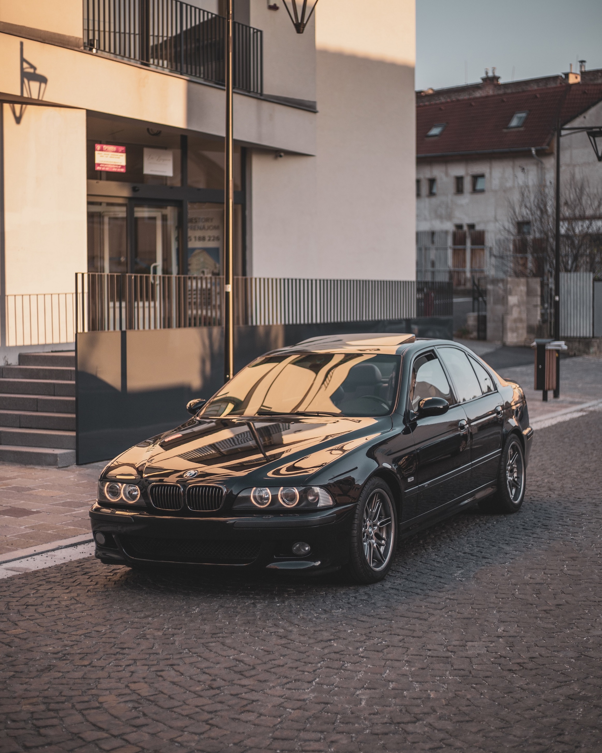 A black post-facelift BMW E39 M5 sedan parked on a European city street