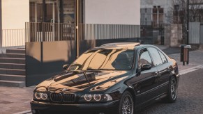 A black post-facelift BMW E39 M5 sedan parked on a European city street