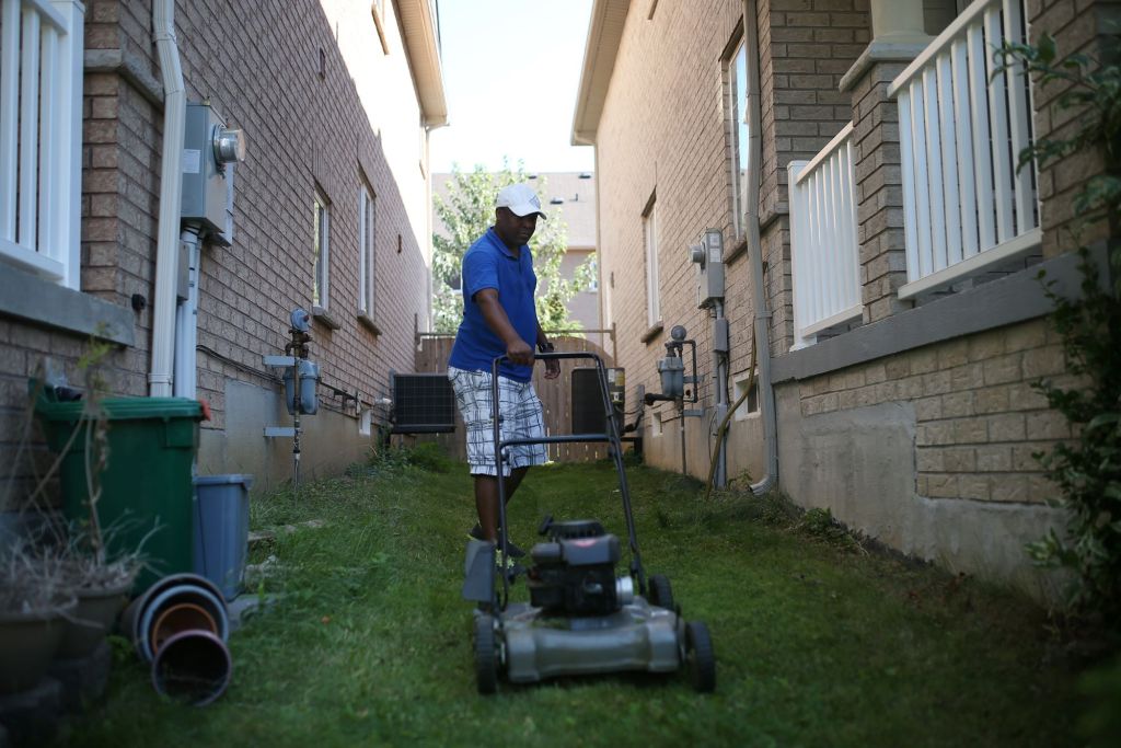 A man with a push mower in an ally way. 