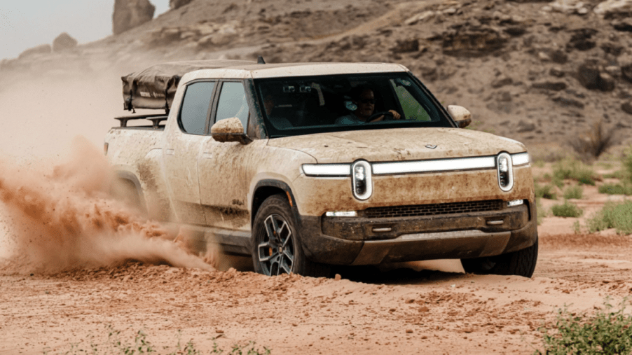 The Rivian R1T all-electric pickup truck model covered in dirt and grime while driving off-road in wet mud and earth