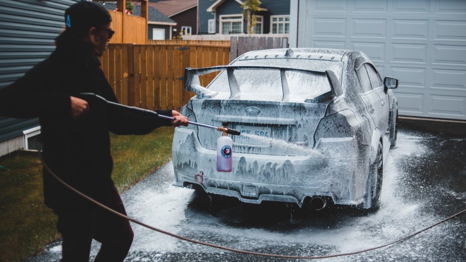 a man covers his car in soap from a foam cannon to get it clean