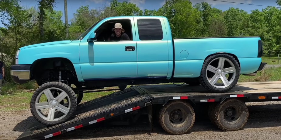 Turquoise-colored squatted Chevy Silverado driving off a transport trailer.