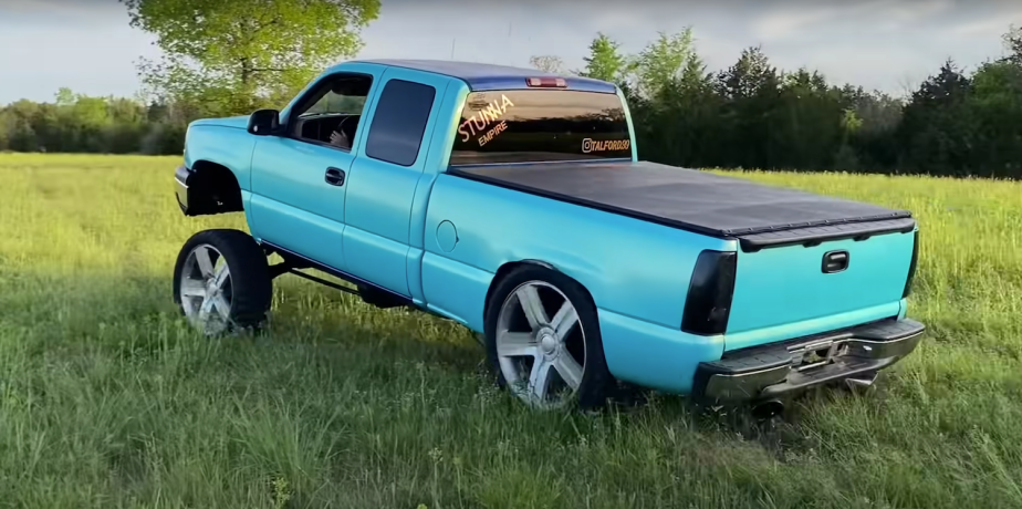 Silverado pickup truck with an aggressive "Cali Lean" or "Tennessee Tilt" lift kit installed, parked in a grassy field.