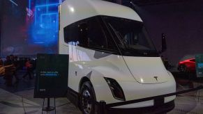 A white Tesla semi-truck parked in an indoor area with blue lights in the background.