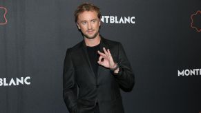 Tom Felton wearing a black suit with a black background.