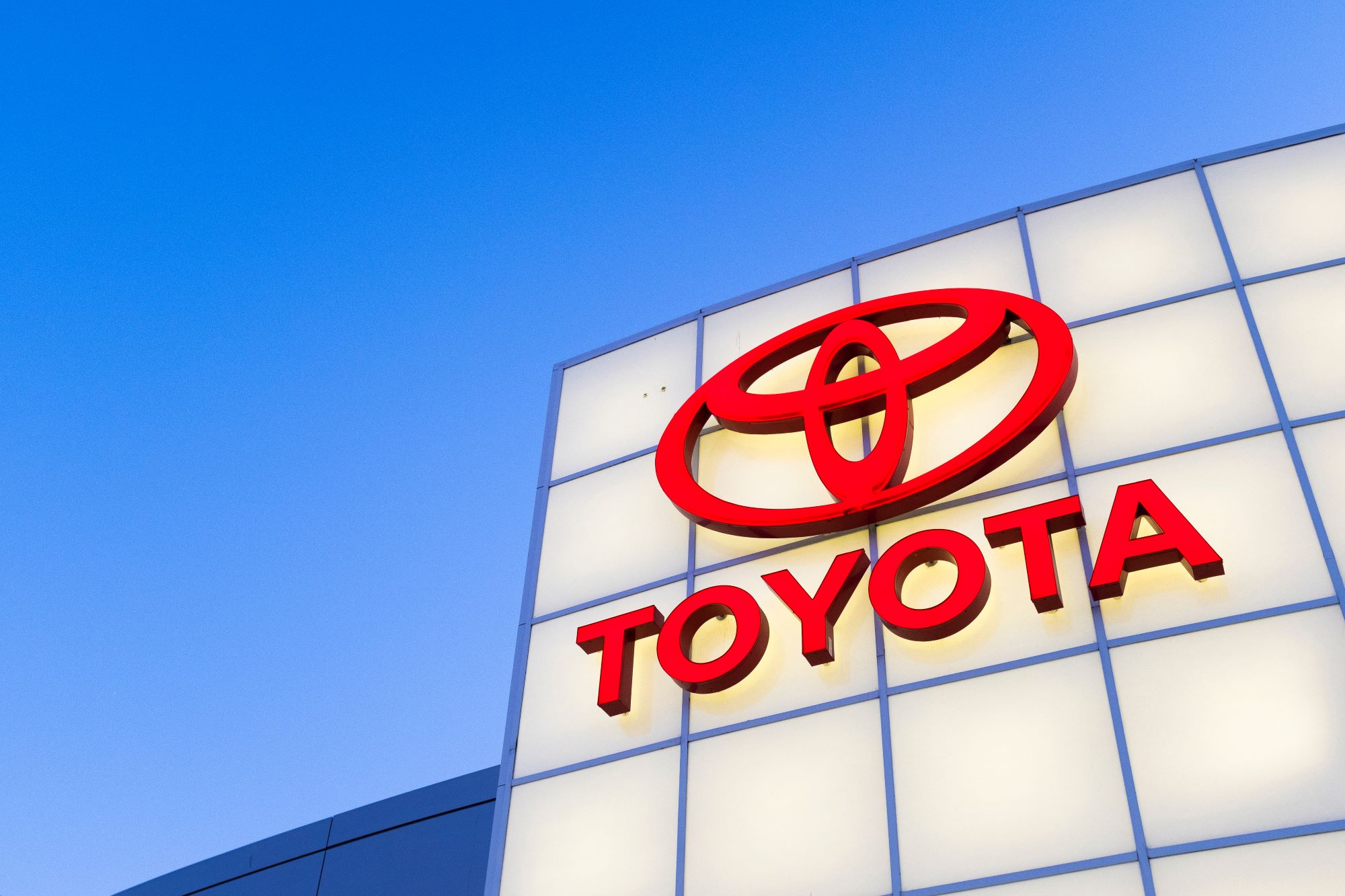 A red Toyota logo with Toyota written under it on a white background with a clear sky in the background.