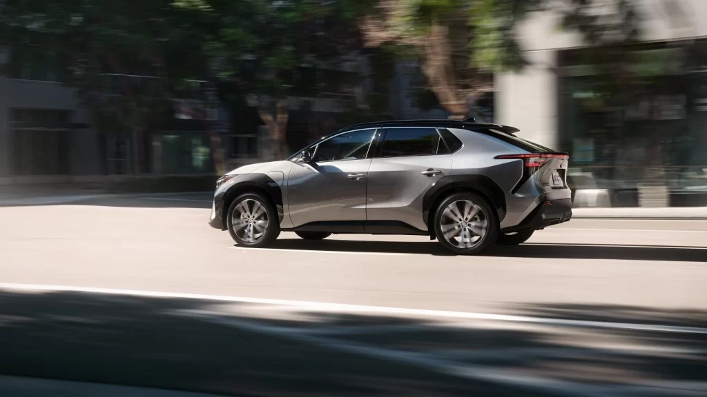 A 2023 Toyota bZ4X with silver paint drives through a city.