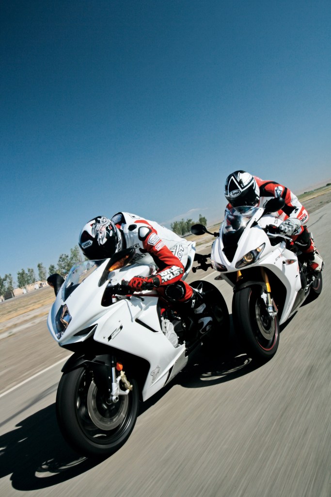 Two riders dressed in bright red-and-white safety gear on white sportbike motorcycles riding down a desert road