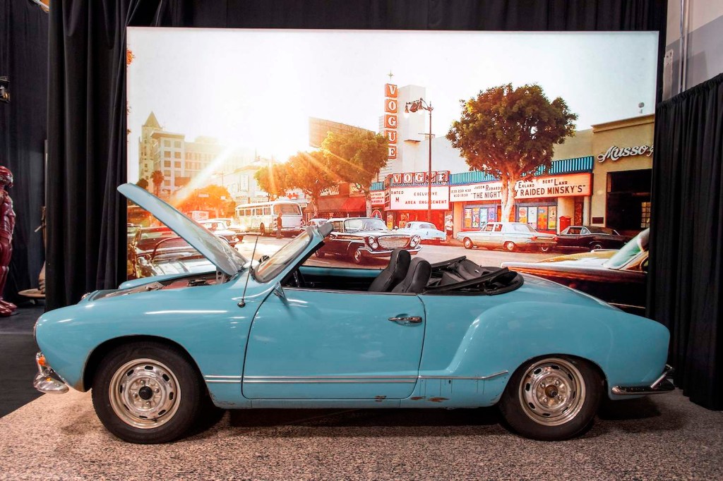 Light blue 1968 Volkswagen Kharmann Ghia used in filming Quentin Tarantino's Once Upon a Time in Hollywood at a charity auction with movie poster in the background.