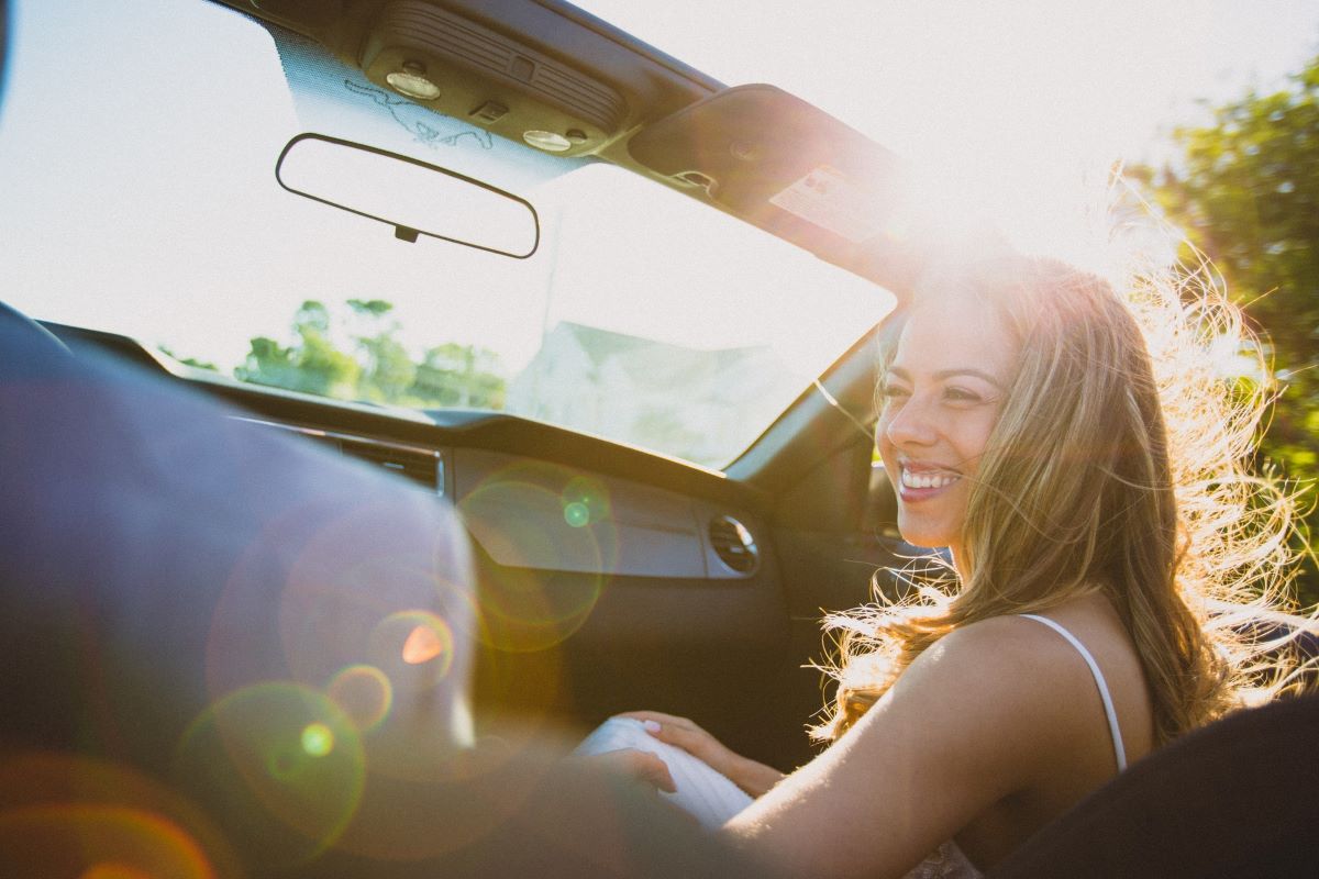 Happy smiling white woman sits in the passenger seat of a summer convertible with the top down