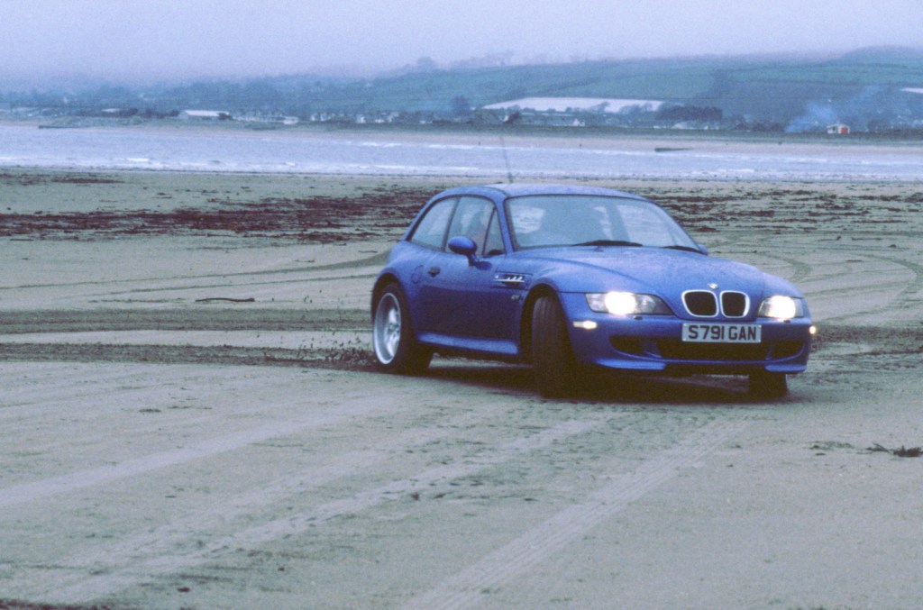 The discontinued BMW Z3 M Coupe is shown driving through sand.