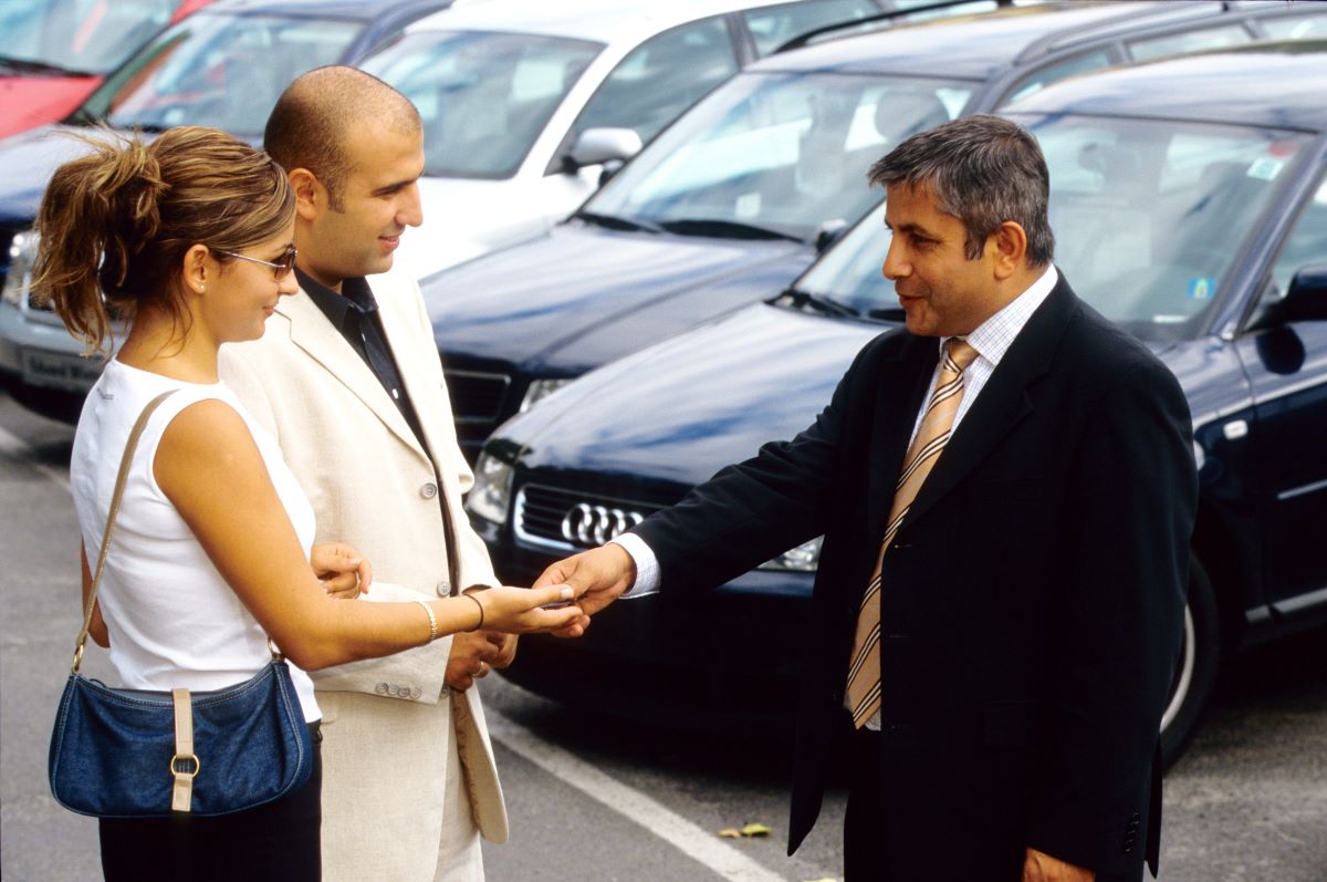 Couple accepting a car key from a car salesman. Car-buying roadblocks can often start at the dealership