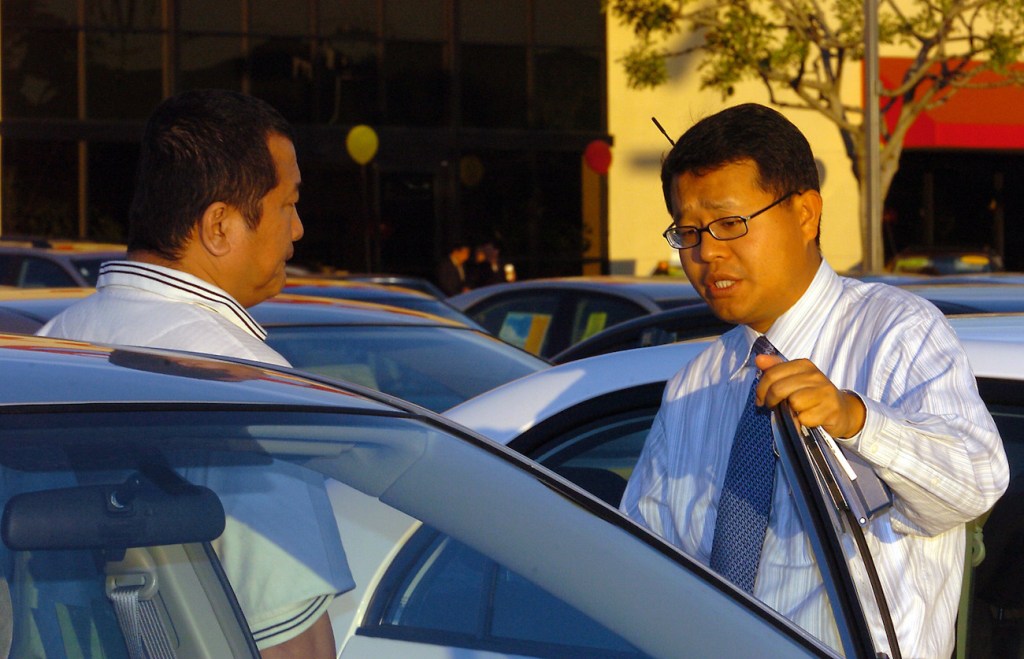 A salesperson talks to a customer at a car. 