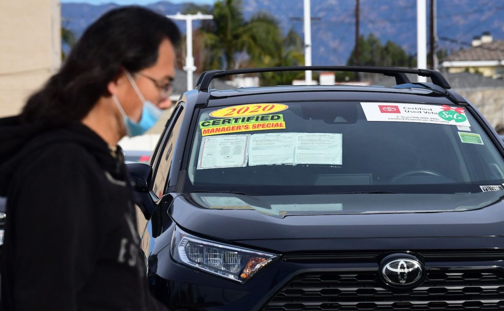 A pedestrian walks past a certified pre-owned car sales lot 