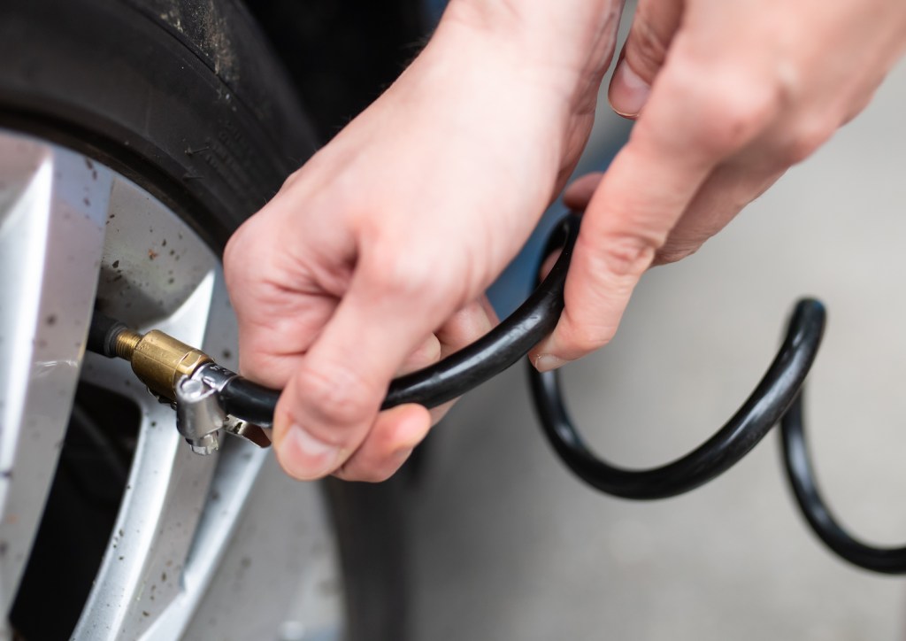 A woman checks the air pressure on a car tire at a gas station.