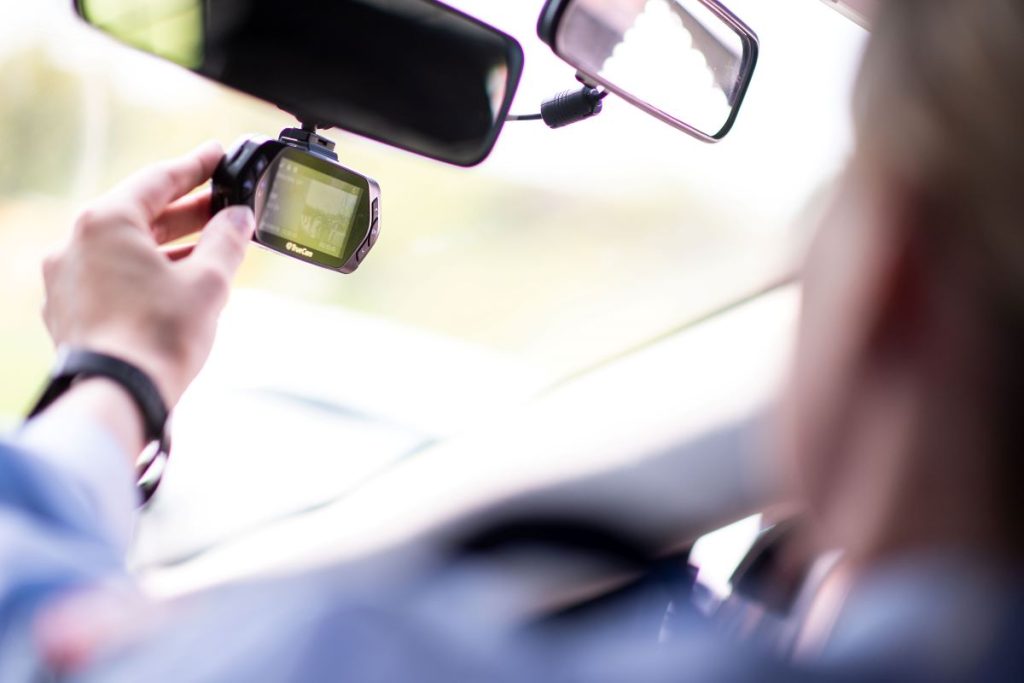 A person adjusts a dashcam that is mounted on the front windshield just below the rearview mirror. In-car cameras can help with insurance claims