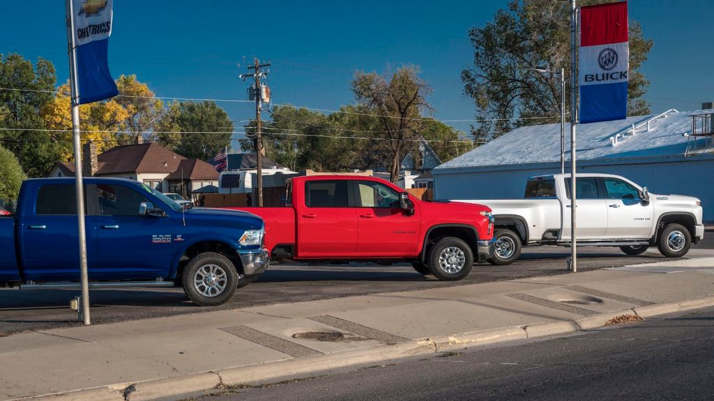 Blue Ram truck, Red Chevrolet truck, and white GMC pickup truck lined up at a used car dealership.