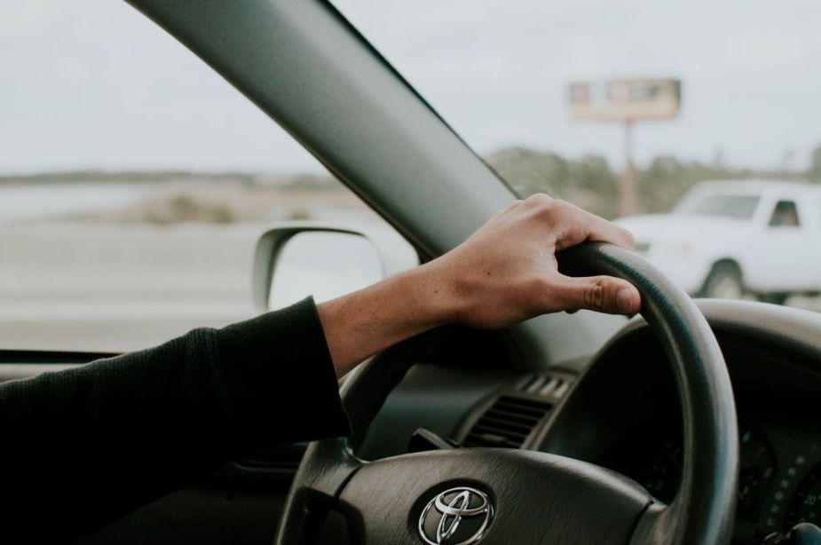 Hand resting on the steering wheel of a Toyota vehicle. It is ok to drive a Toyota with the maintenance required light on.