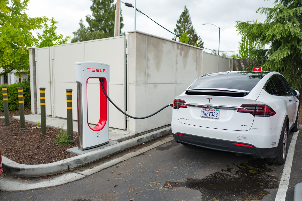 A white Tesla Model X charging at a supercharger EV charging station