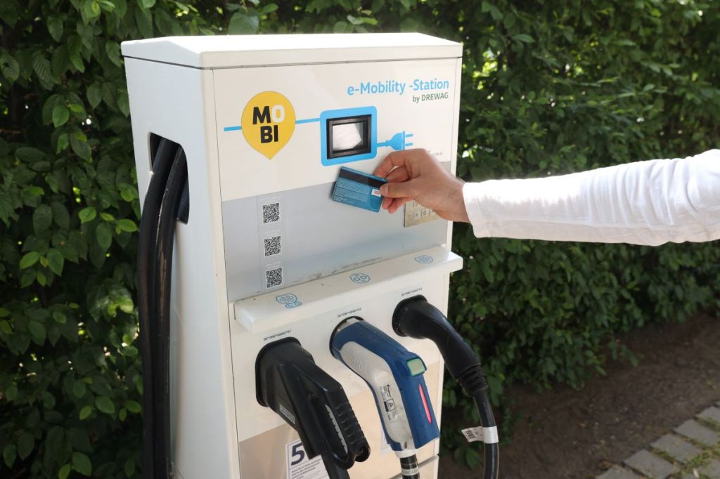 A person holds their credit card against an EV charging station, presumably to pay for charging services