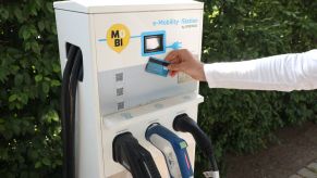 A person holds their credit card against an EV charging station, presumably to pay for charging services