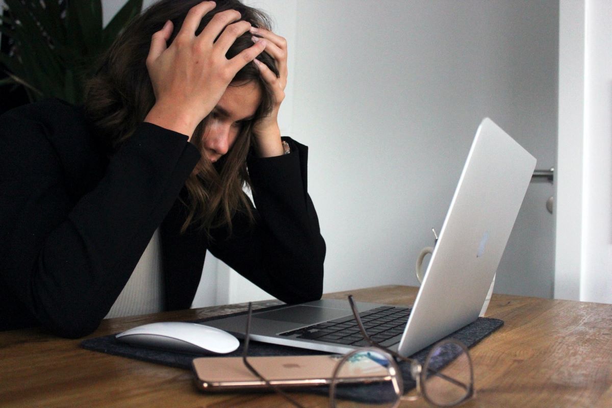 Person with medium length brown hair sitting at their computer. They're holding their head in frustration. Car-buying roadblocks can cause confusion.