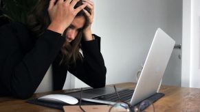 Person with medium length brown hair sitting at their computer. They're holding their head in frustration. Car-buying roadblocks can cause confusion.