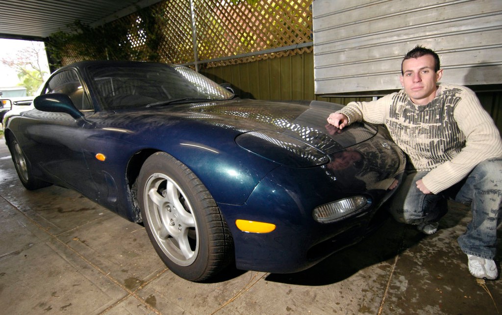 A man sits next to his FD Mazda RX-7.