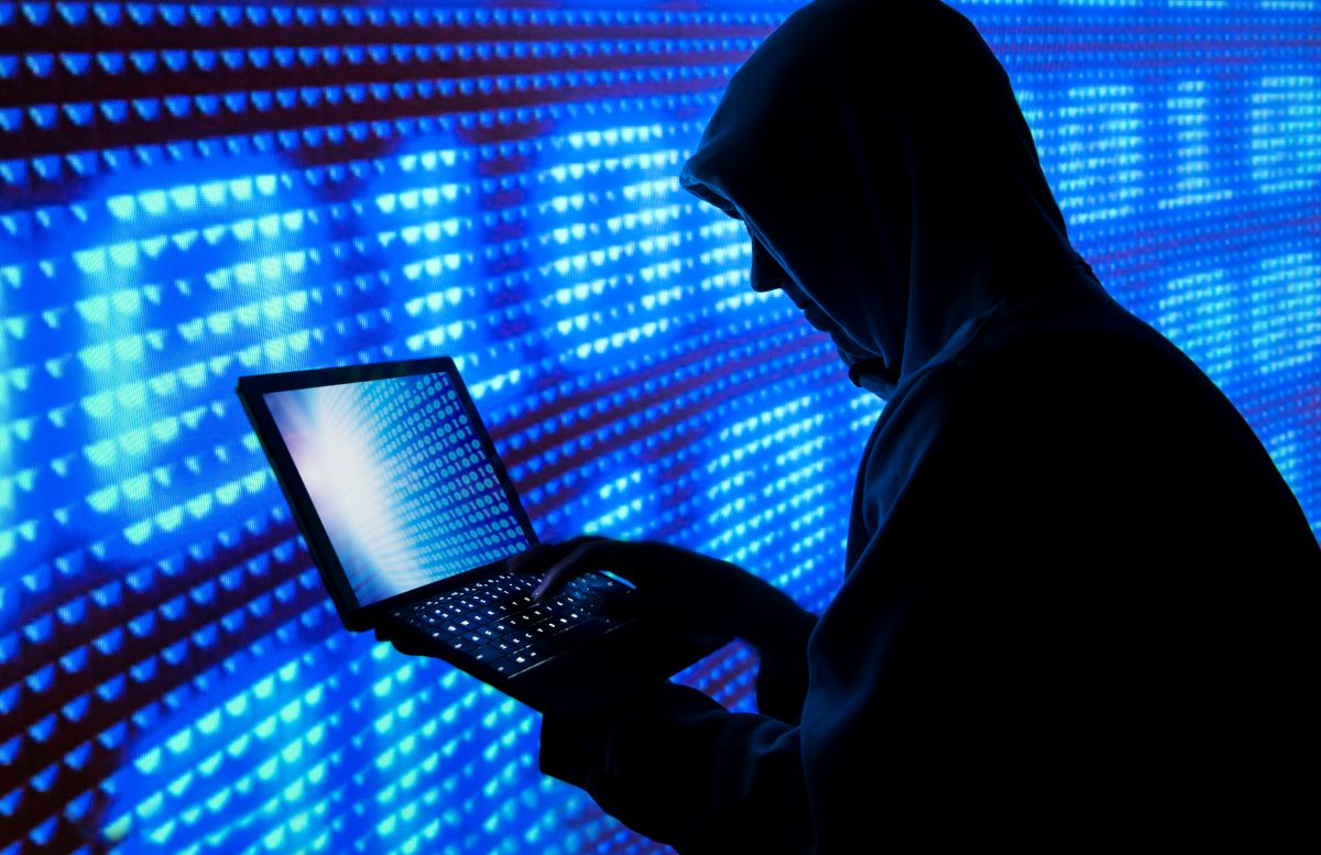Silhouette of a hacker wearing a hoodie and holding a computer; hackers are targeting EV charging stations
