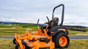 Orange, Scag riding lawn mower parked above a road and town.