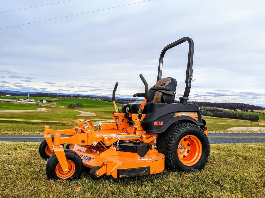 Orange, Scag riding lawn mower parked above a road and town.