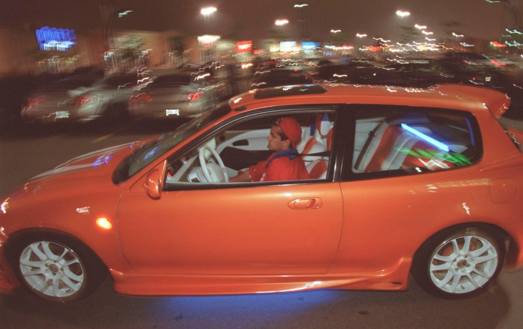 A lowered orange Honda Civic drive through a parking lot.