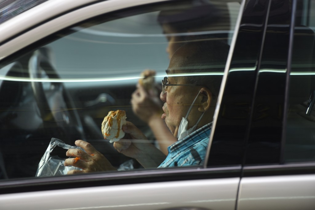 Two men eat their take away food inside a car. 