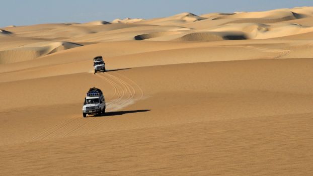 Off-road vehicles driving over and through sand dunes in the Sahara desert in Egypt