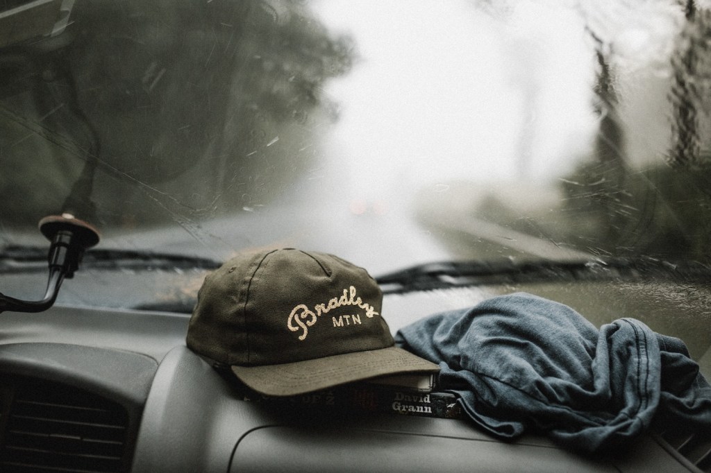 A baseball cap on the dashboard of a car that's driving through the rain.