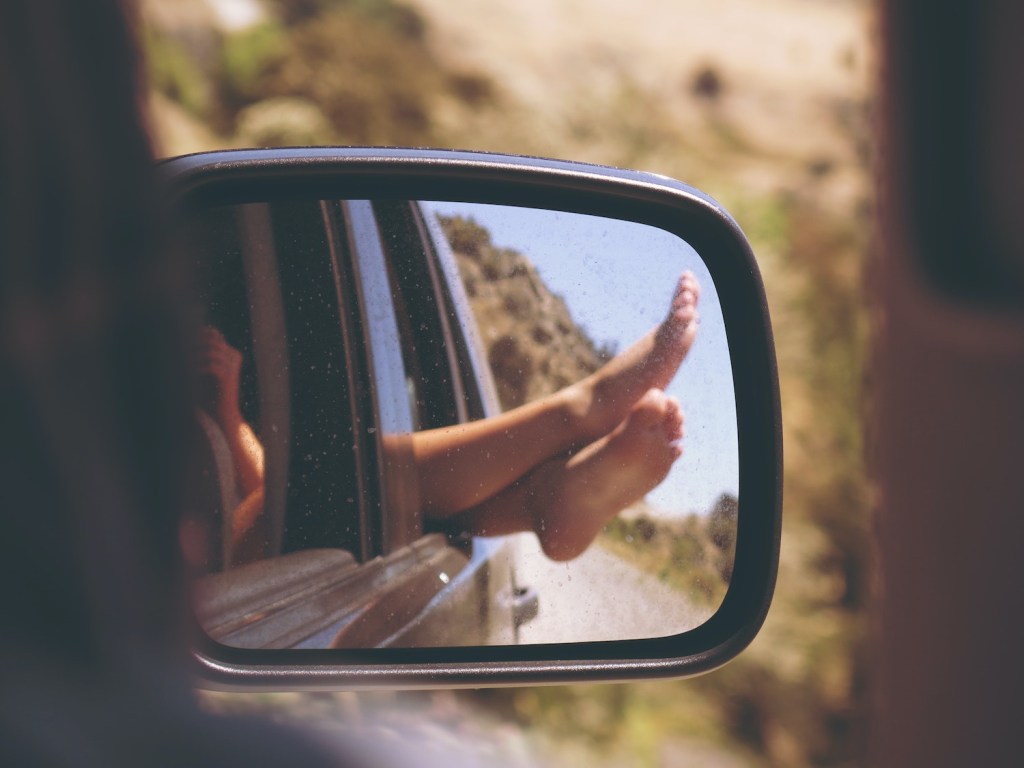 A passenger hangs their feet out the window of a hot car while its driving.
