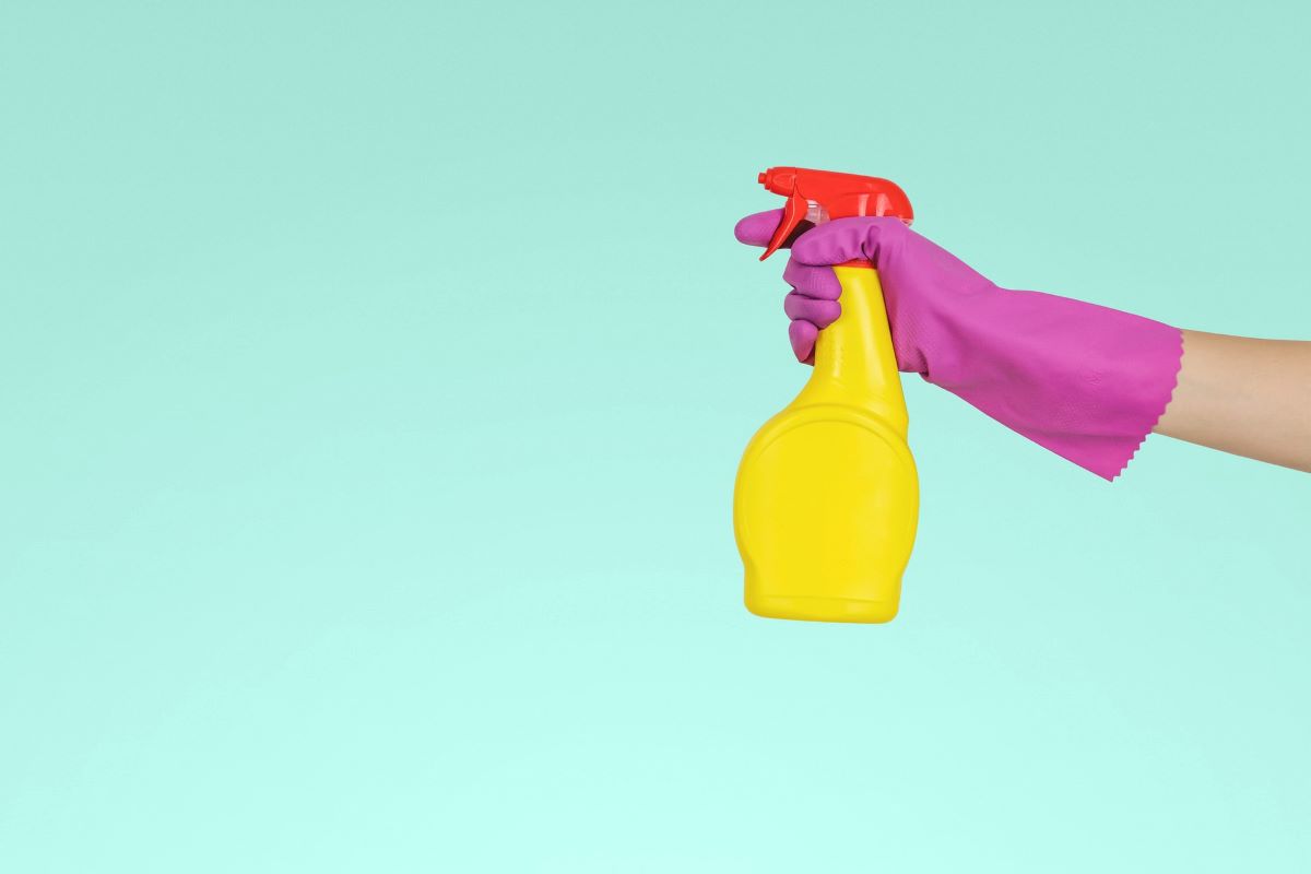 A hand wrapped in a pink glove holds a yellow spray bottle with a red top