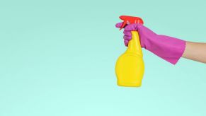 A hand wrapped in a pink glove holds a yellow spray bottle with a red top